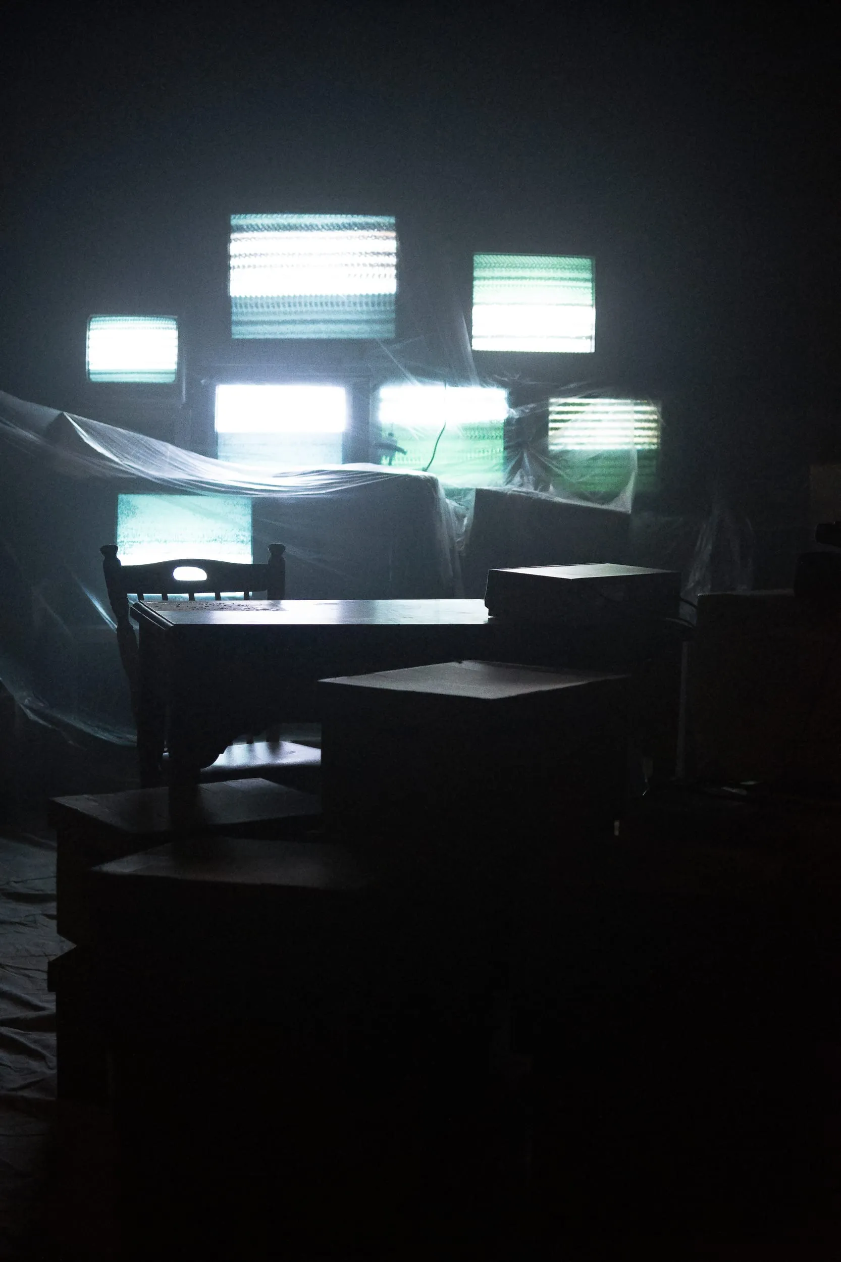The den in cold half-light: desk and chair silhouetted against stacked televisions flickering with static