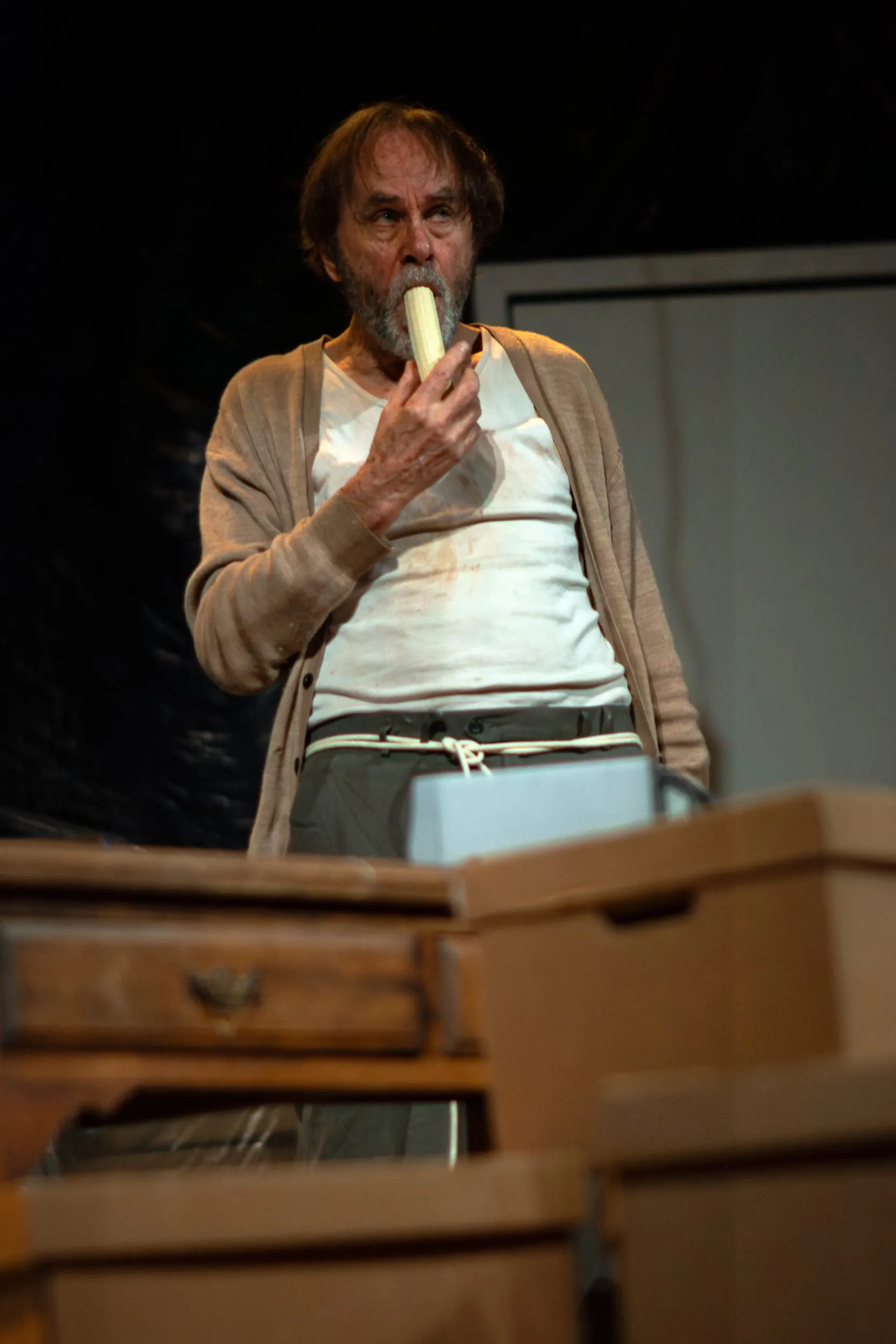 Krapp eats a banana amid the drawers and boxes of his den