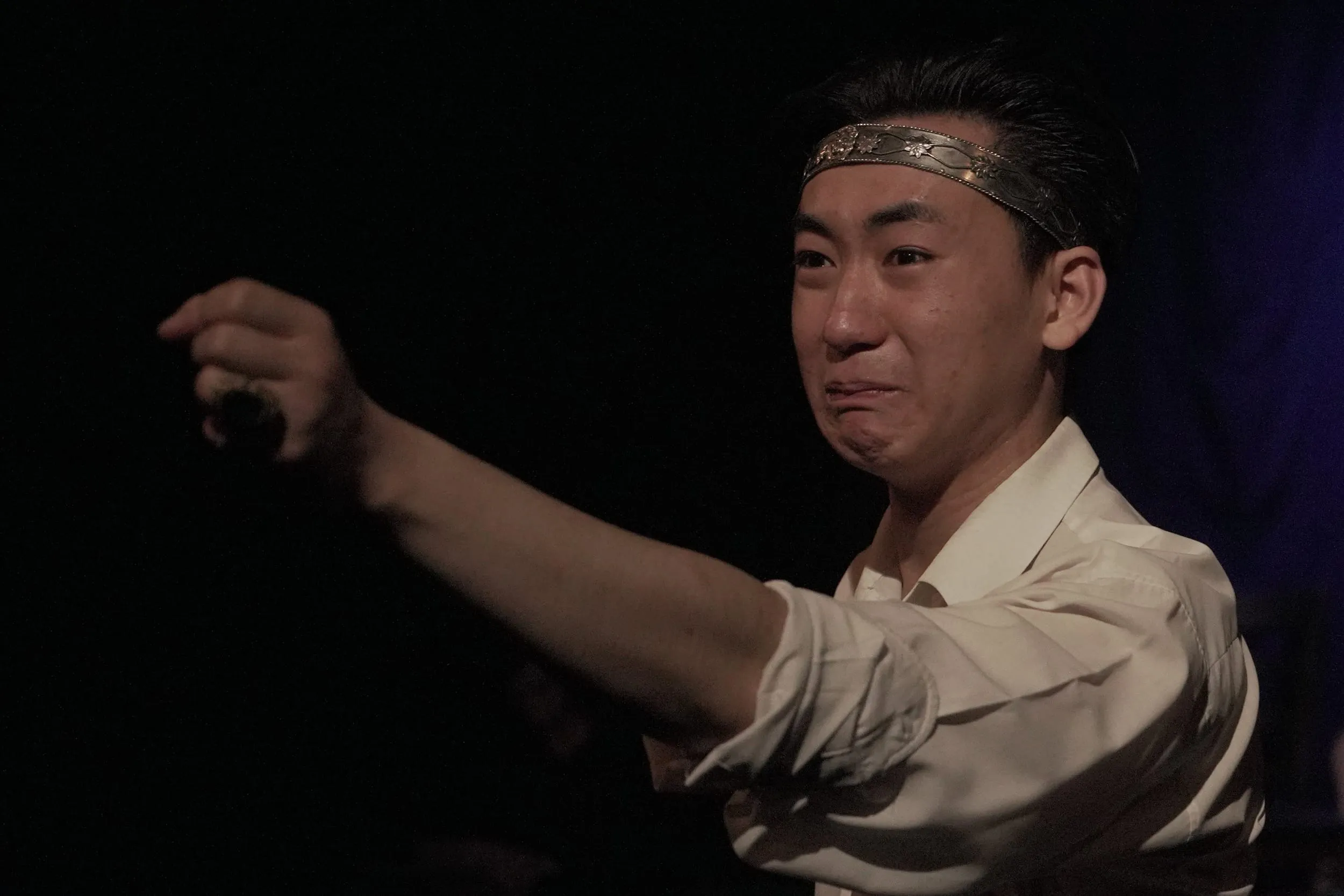Macbeth, crowned with a silver band, grimaces as he draws a dagger forward