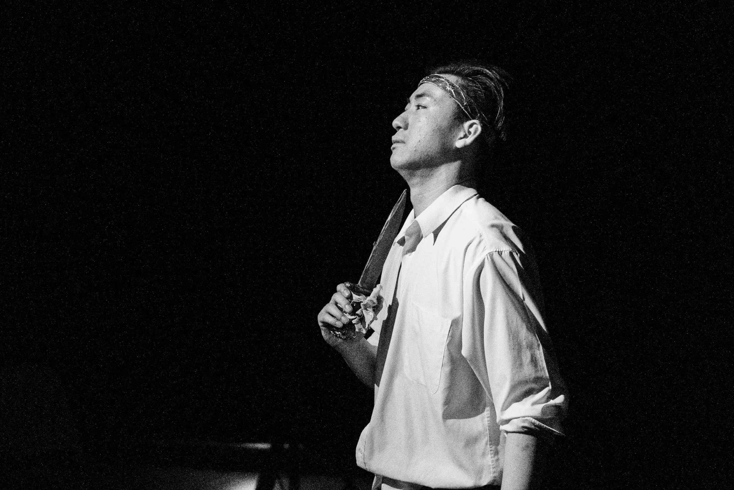 Black-and-white: Macbeth in shirtsleeves holds the dagger to his shoulder, gazing upward