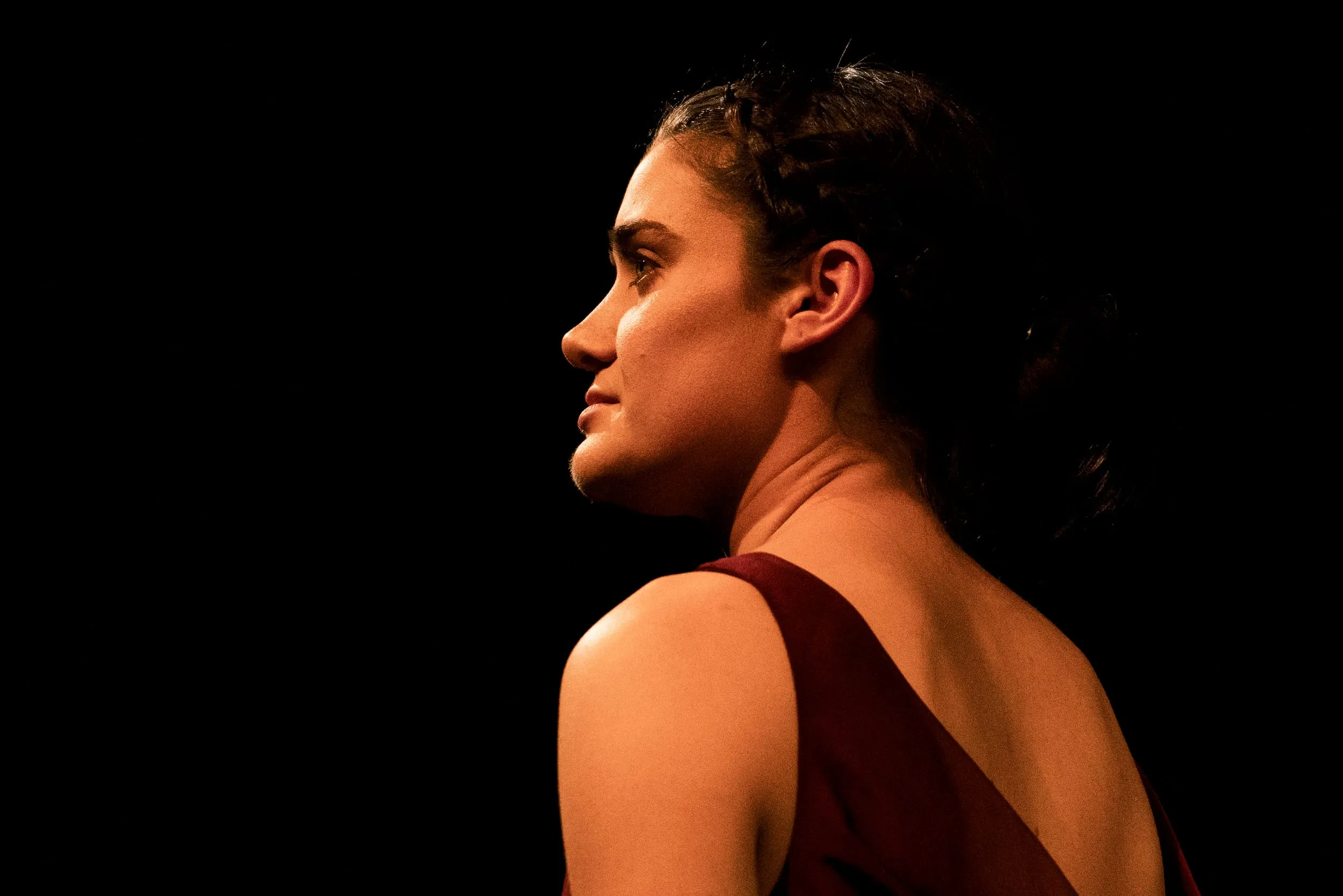 Lady Macbeth in profile against the dark, braided hair catching a sliver of light