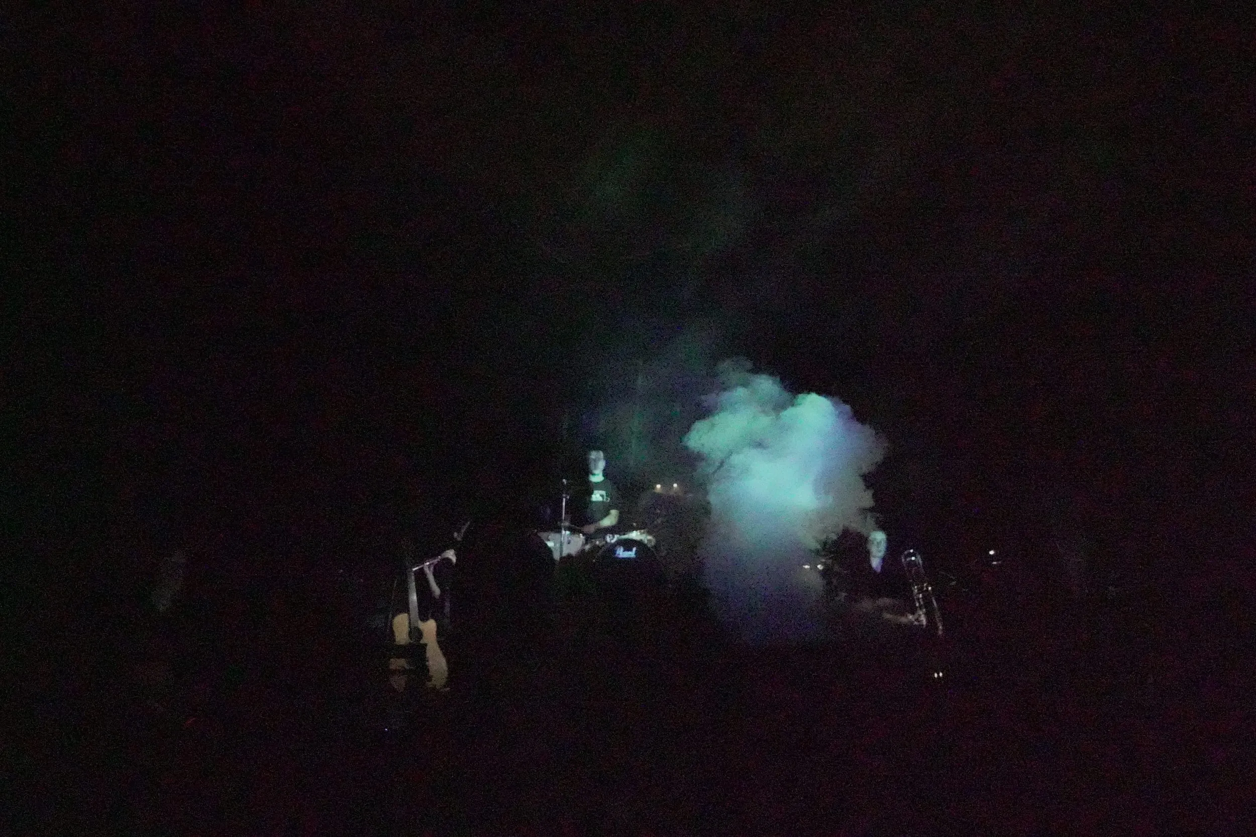 Smoke drifts through the darkness over the dim silhouettes of the band