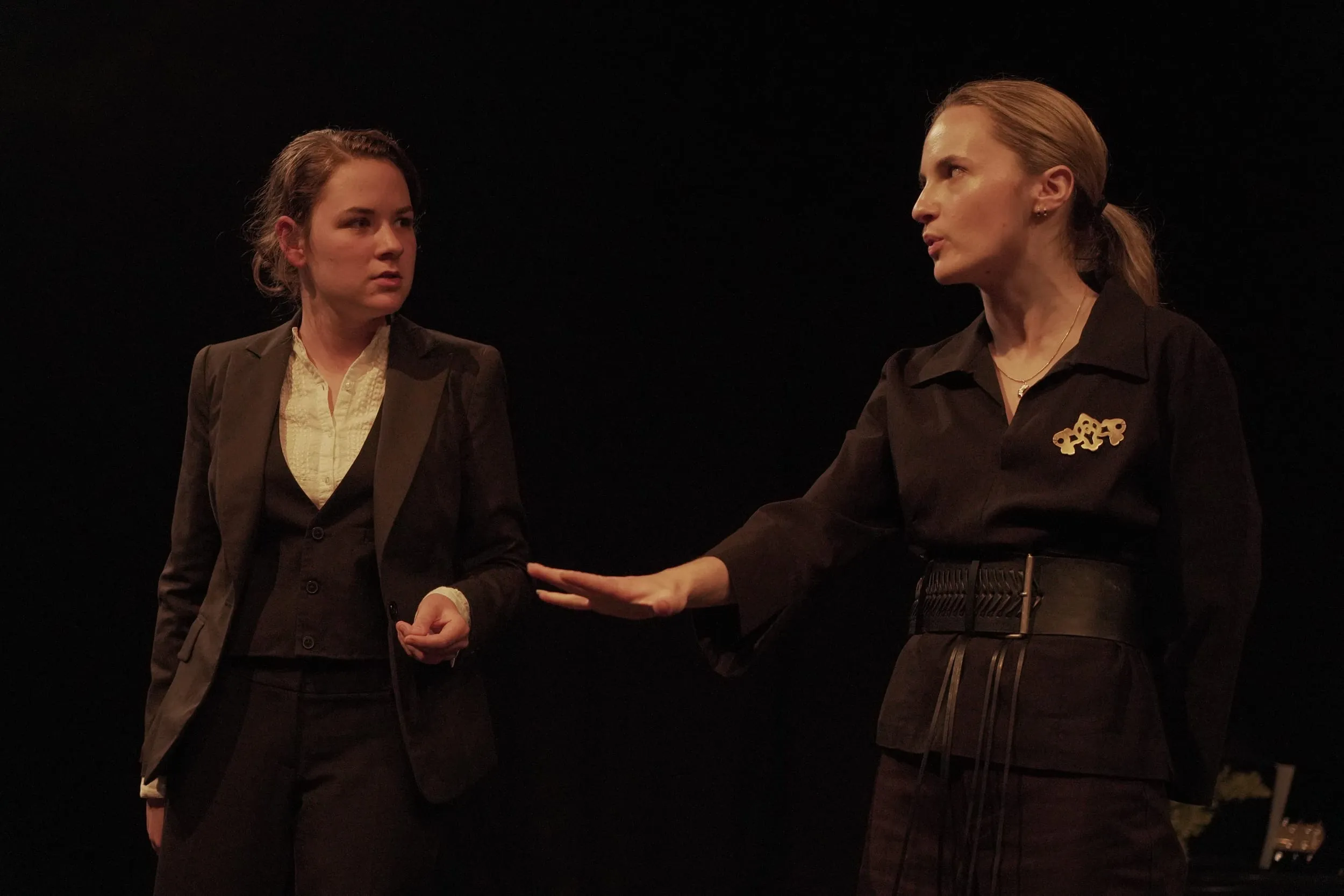 Two women in black — one suited, one belted — face each other mid-confrontation