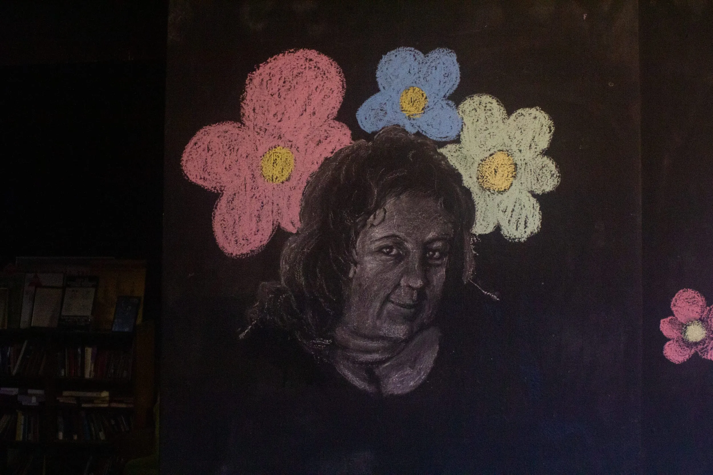 A chalk portrait of the performer's mother on a black wall, crowned with pink, blue and white chalk flowers