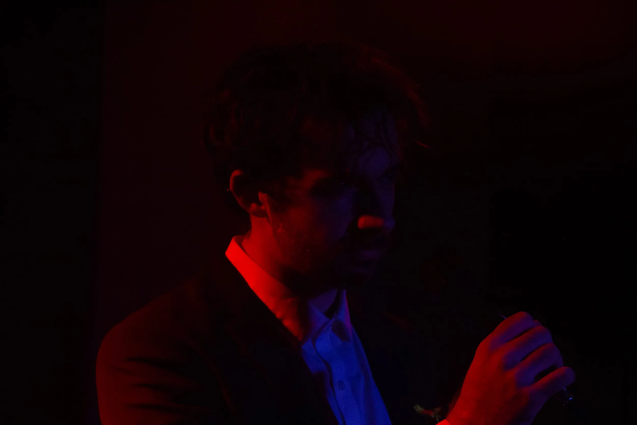 The performer clutches the microphone in near-darkness, lit half red, half blue