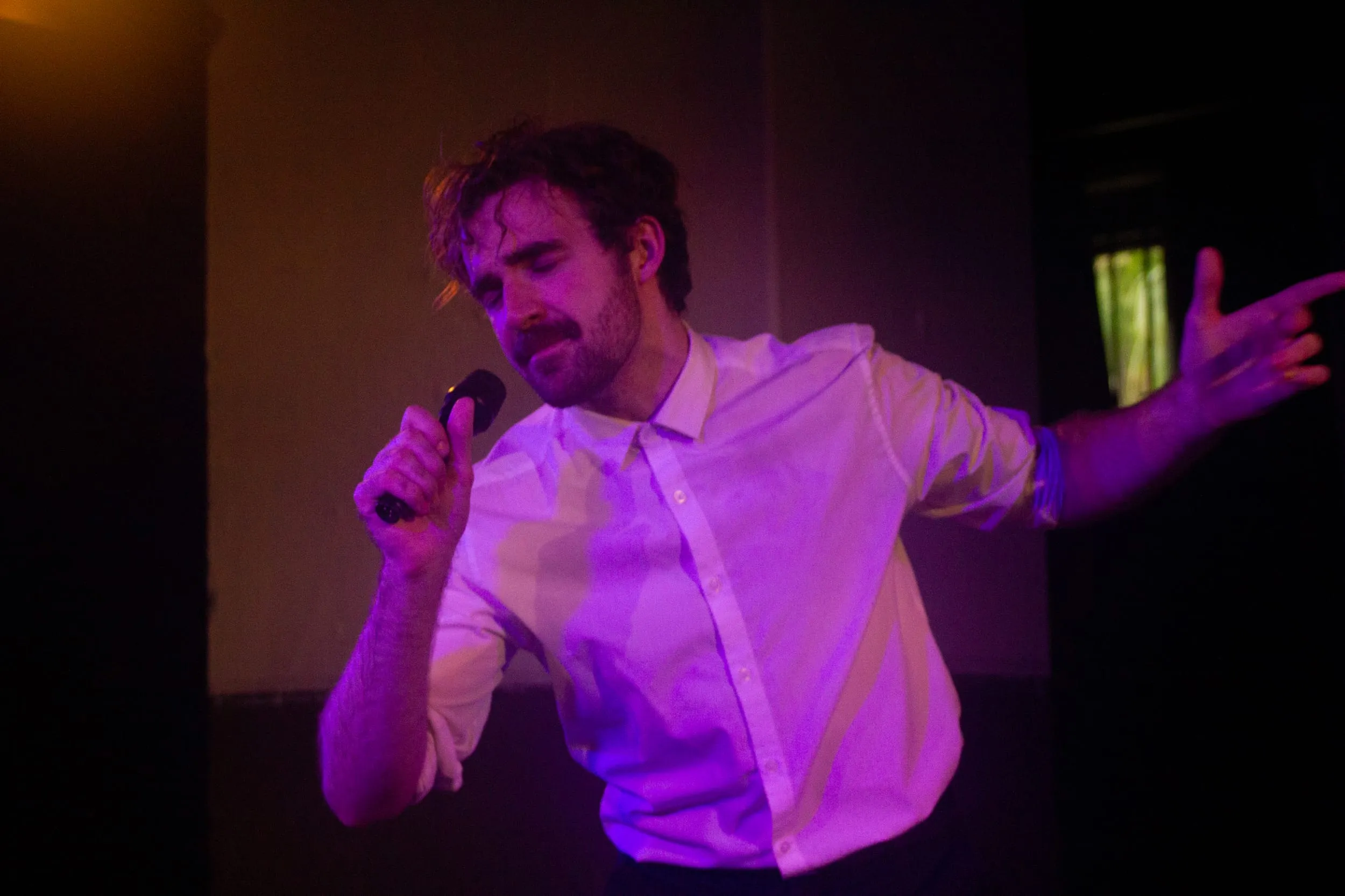 The performer belts into the mic under pink light, free arm flung wide