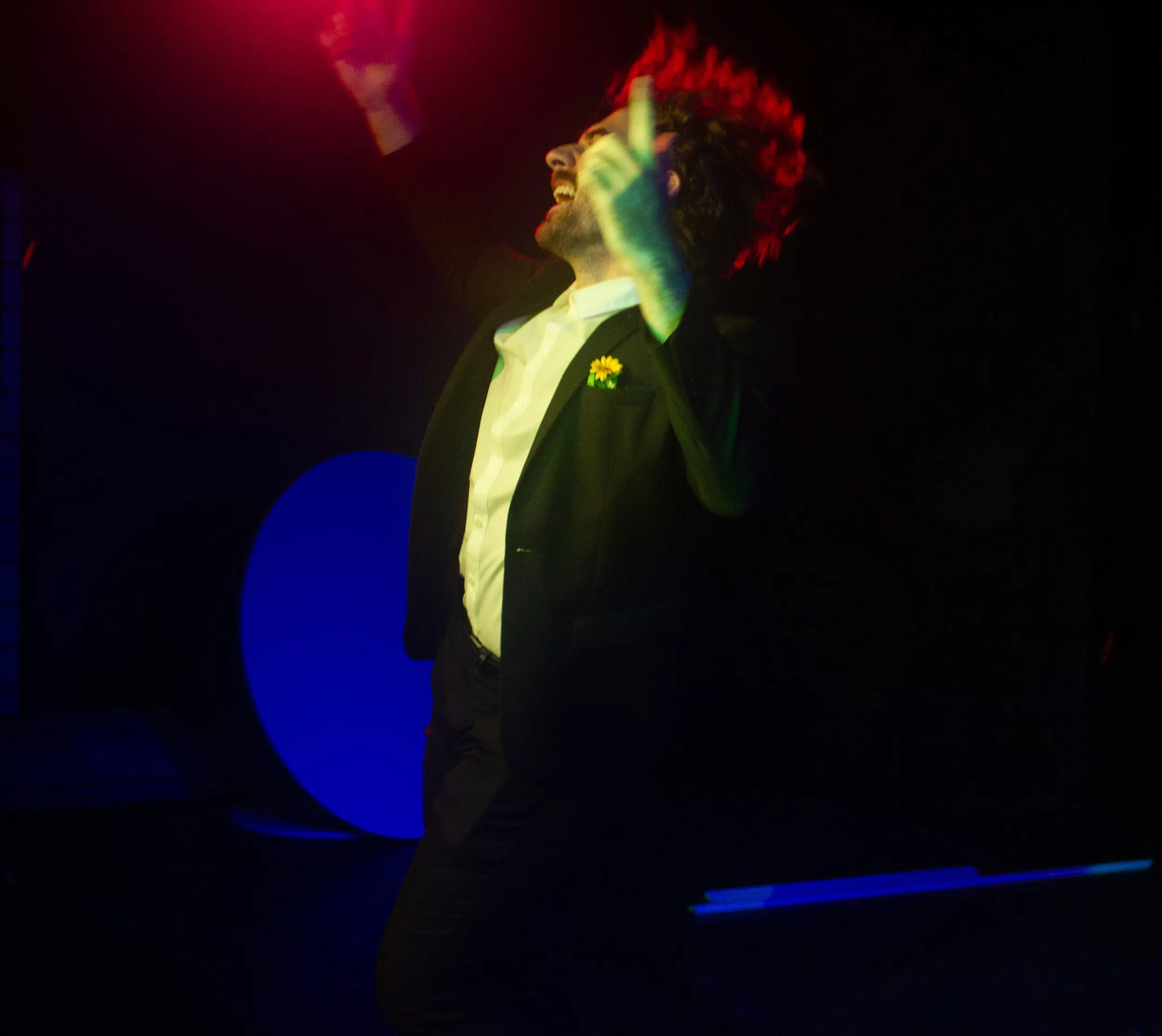 Caught in motion blur, the performer throws a fist skyward against red and blue light