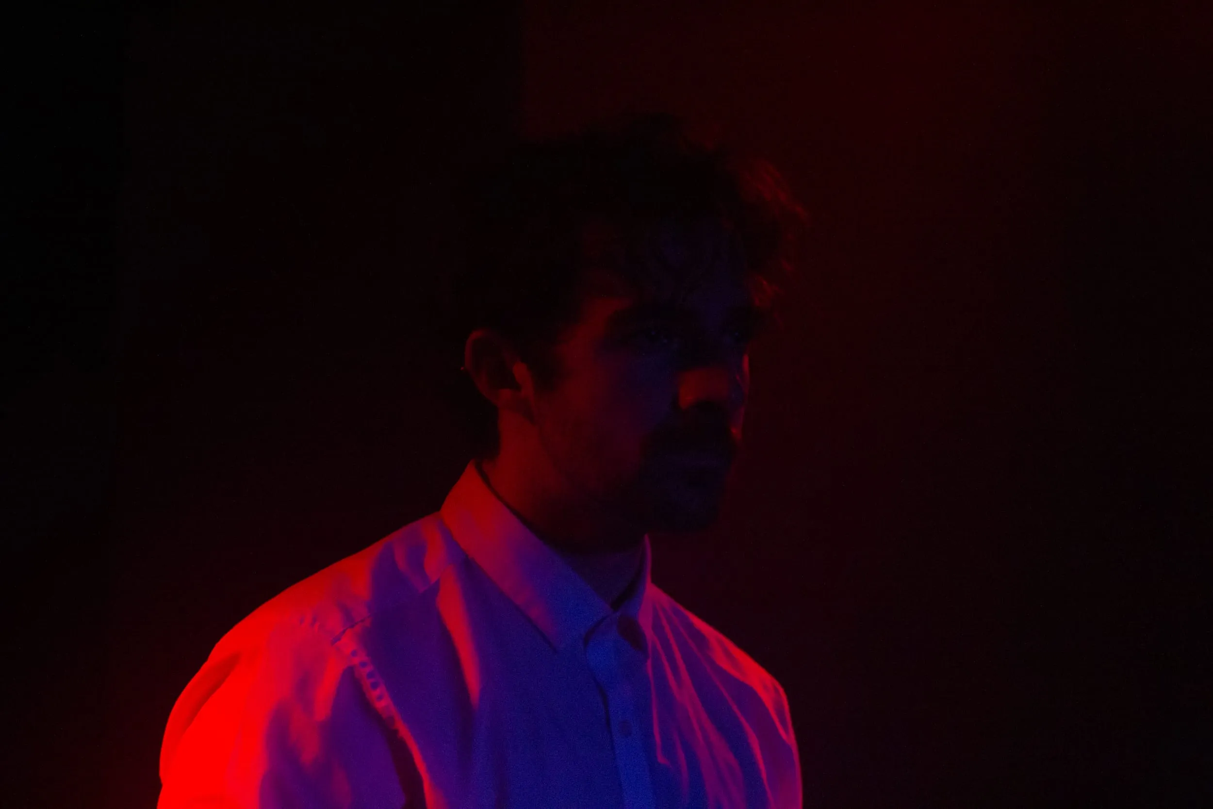 The performer stares into the dark, face rimmed in red light
