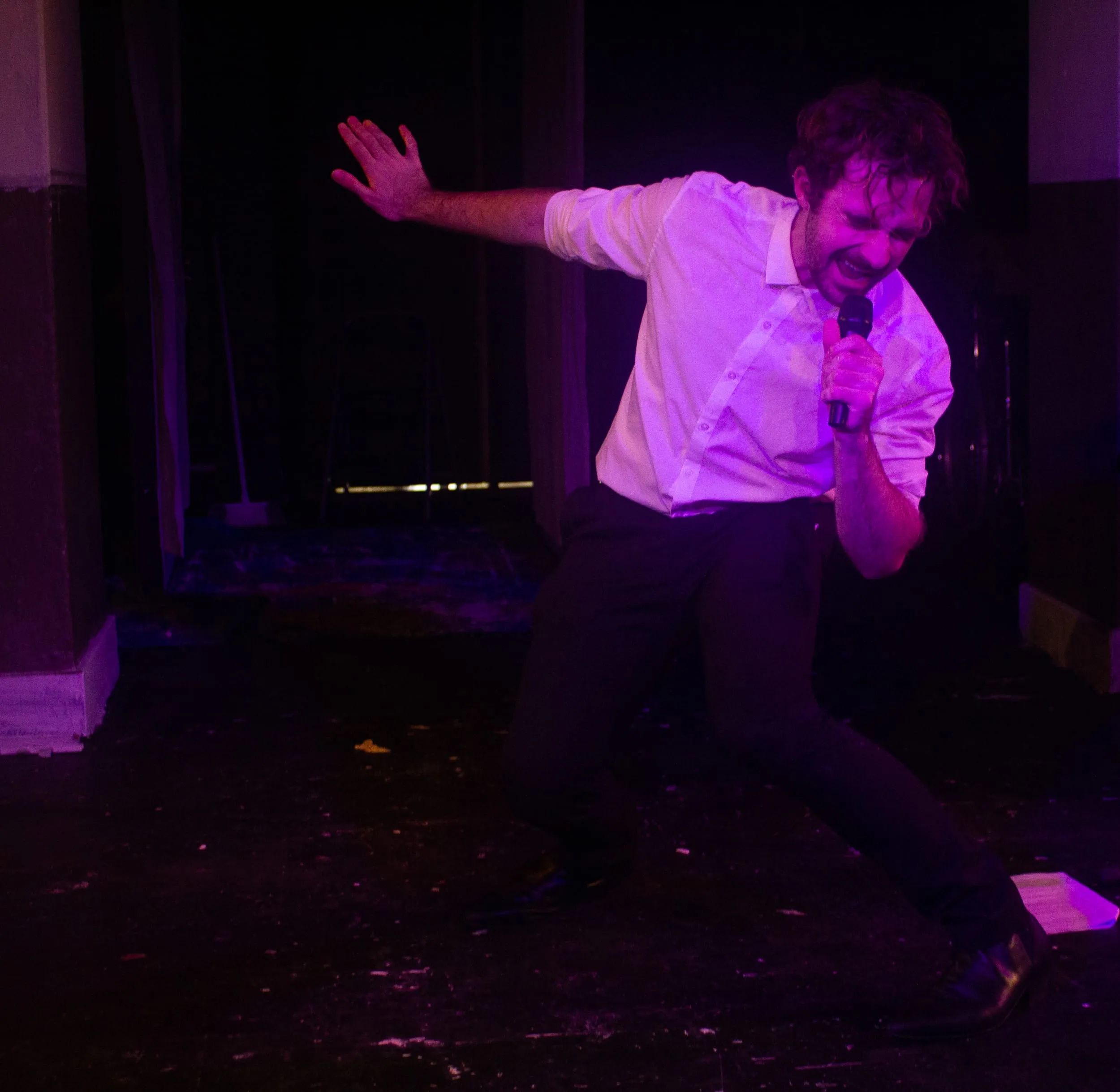 The performer lunges low across the stage, mic in hand, under purple light