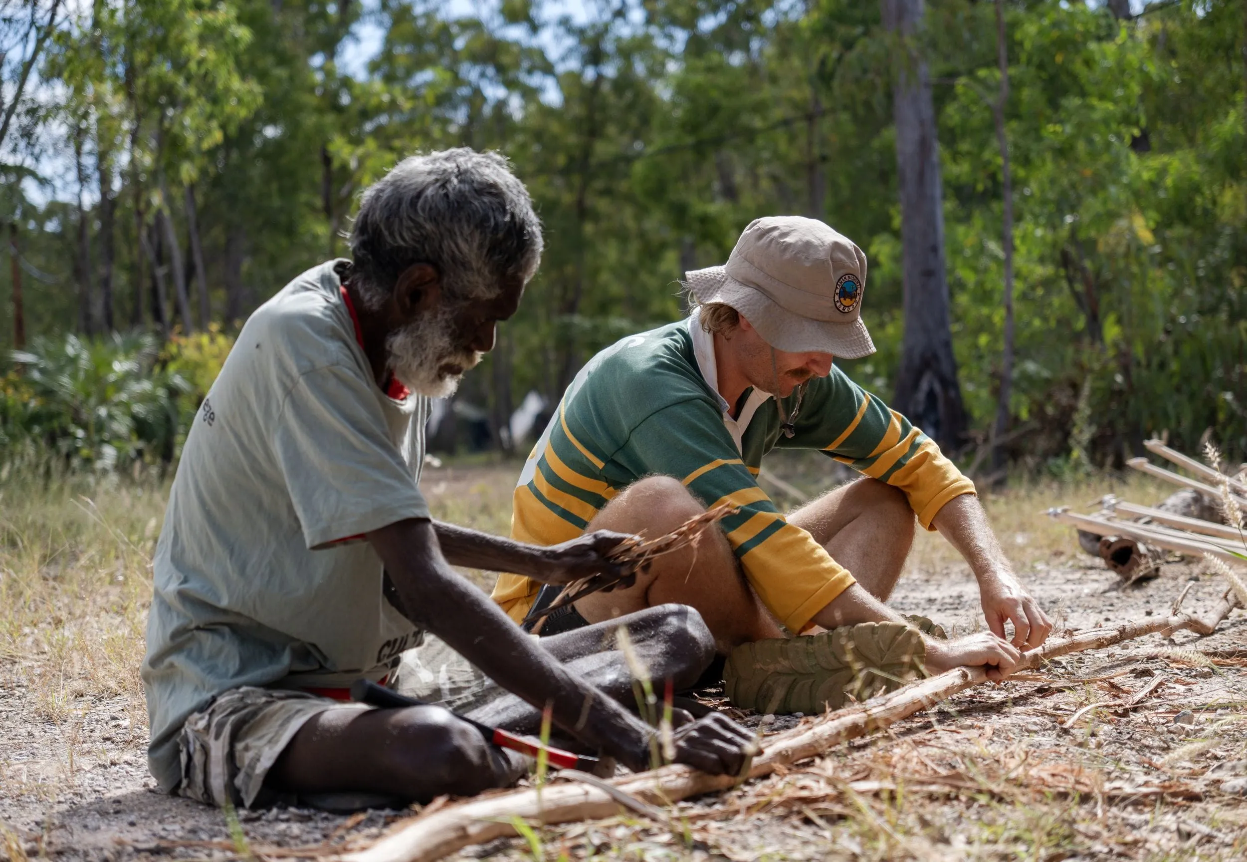 Two men sit on the ground shaping wooden spears together, Arnhem Land