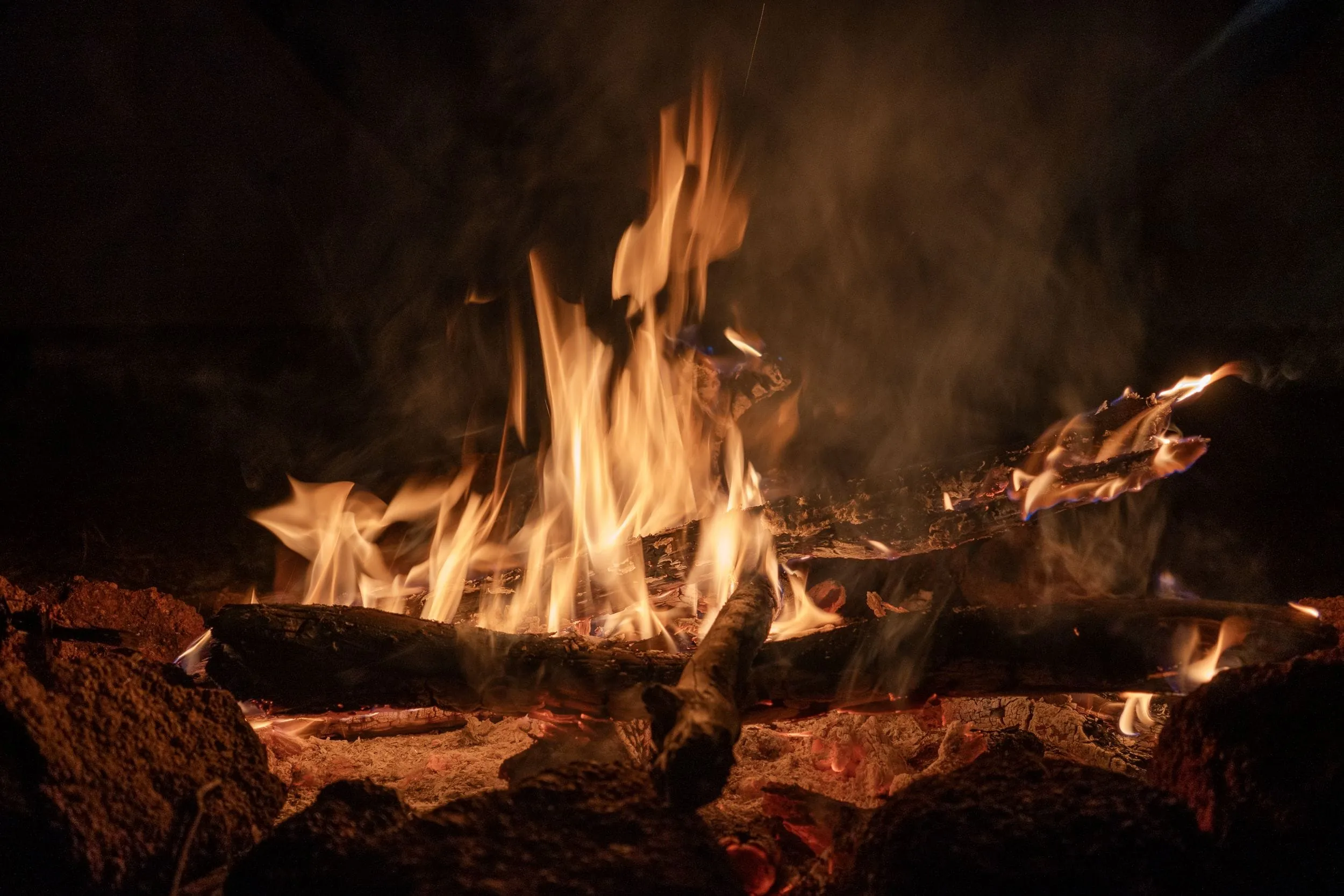 Flames curl over a campfire at night