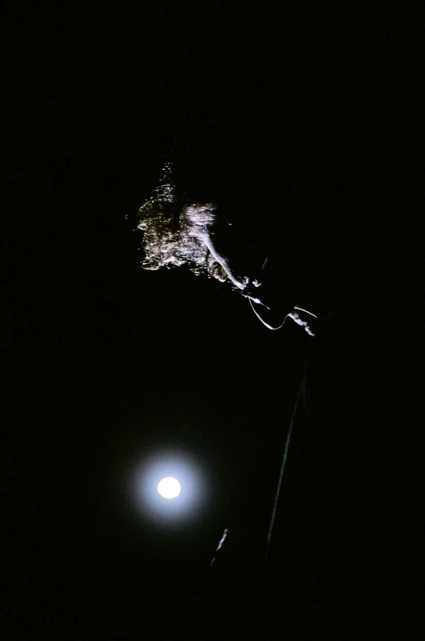 A performer suspended in darkness above a glowing full moon — lighting design for The Birthday Party (2018)