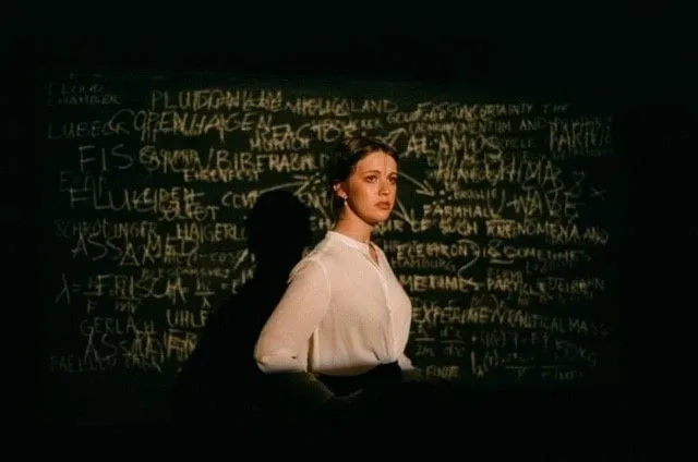 An actor lit in a single warm pool before a chalked blackboard — lighting design for Copenhagen (2019)