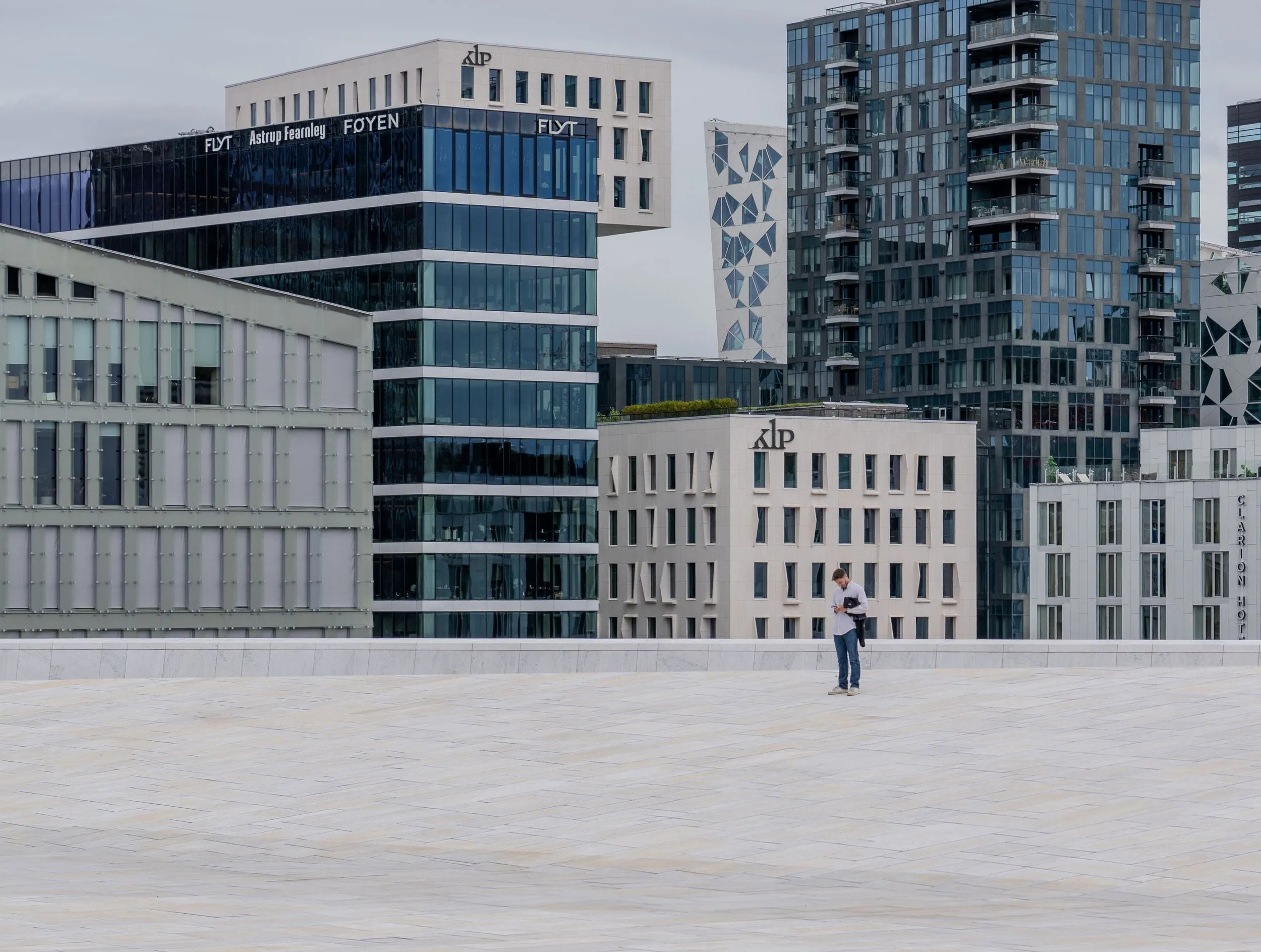 A lone figure crosses the white marble roof of the Oslo Opera House beneath glass towers
