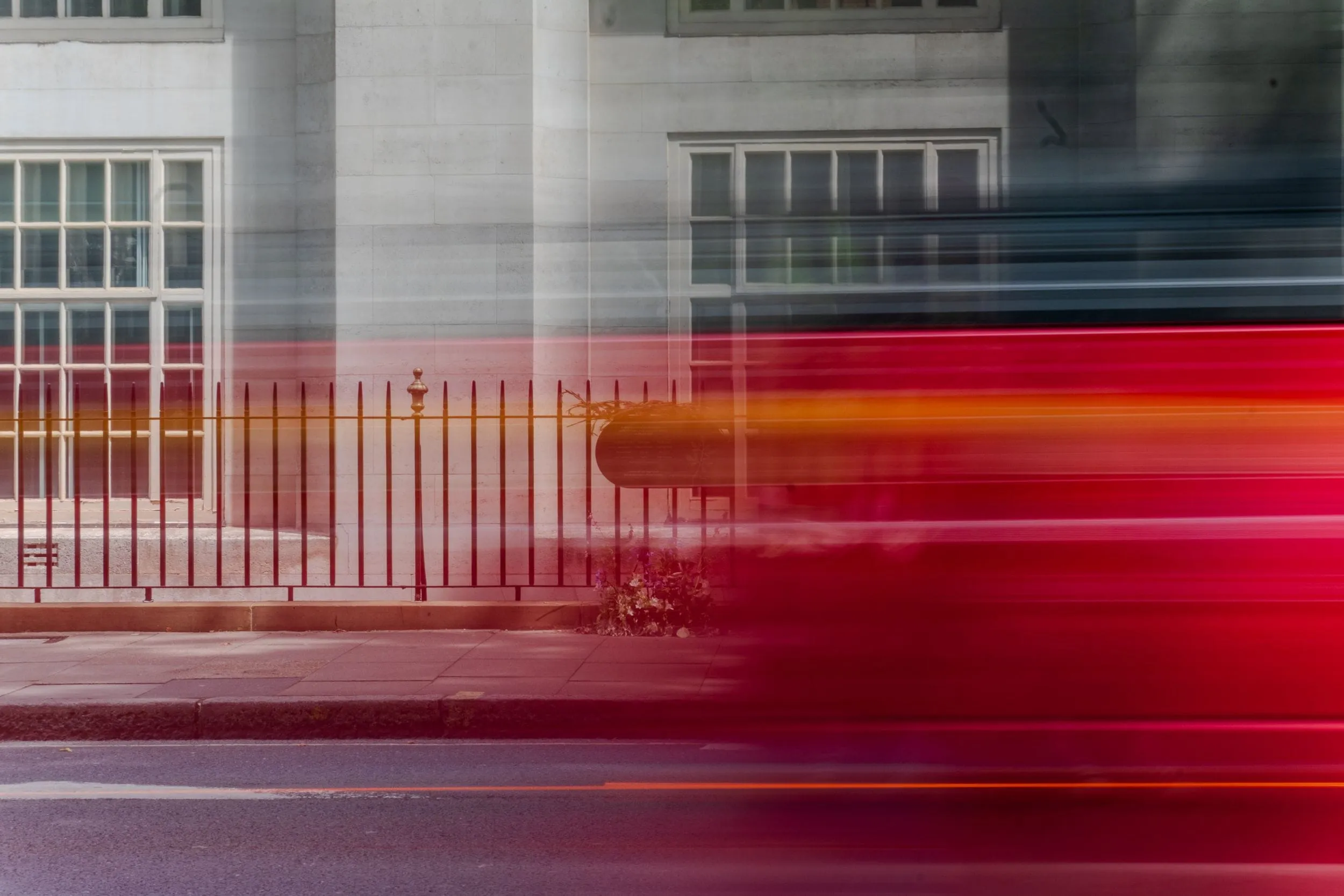 A red London bus streaks past iron railings in a long-exposure blur