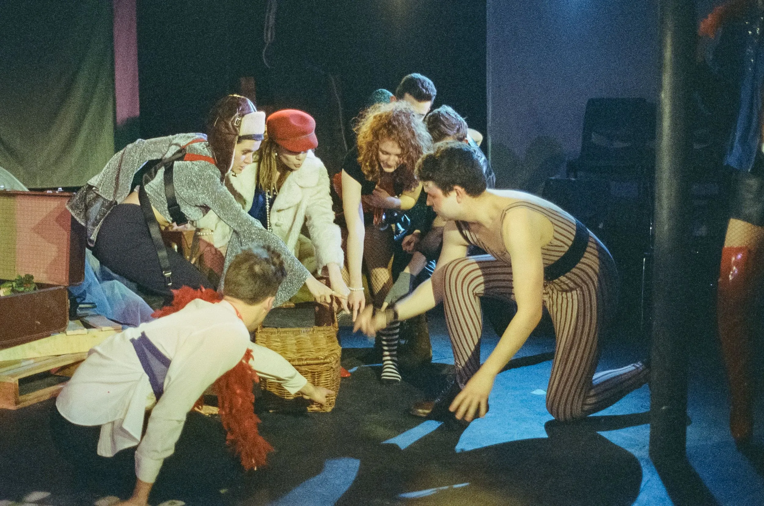 The travelling players rummage through a wicker prop basket in their patchwork costumes