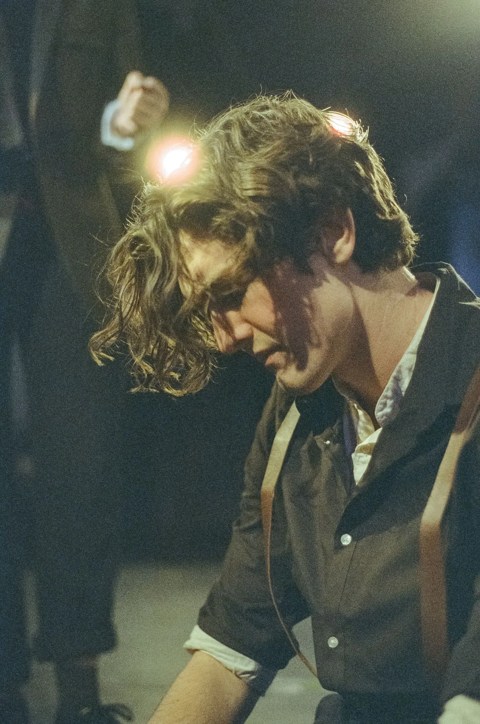 A performer bows his head in the half-light, curls falling over his face